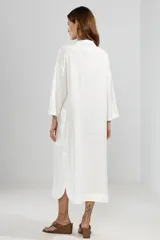 Camisa larga blanca de lino 100% italiano, con cuello clásico, mangas 3/4, silueta fluida, dobladillo curvado en las costuras laterales y bolsillos discretos.