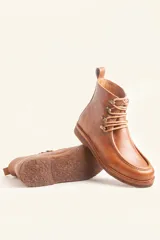 Bota de cuero vacuno color bordó con acabado brillante, diseño tipo botineta con cordones y ganchos metálicos. Presenta suela de goma tipo crepe con plataforma y costuras visibles en la puntera.