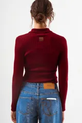 Top de tejido de punto acanalado color negro, de manga larga y cuello polo con botones frontales.