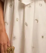 Vestido midi evasé sin mangas, confeccionado en tricolina color blanco, con escote recto con volantes y bordados metalizados de iconos.