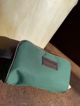 Neceser de lona verde con detalles en cuero color beige y etiqueta con logo de la marca Sierra Mora.