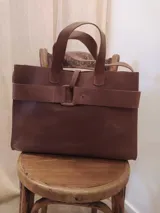 Bolso tote de cuero marrón con doble asa corta y correa ancha horizontal con hebilla.