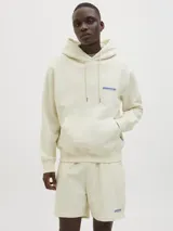 Buzo con capucha color crema, de manga larga y corte holgado. Tiene bolsillo tipo canguro y logo estampado en el pecho.