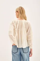 Camisa de manga larga color crudo, confeccionada en viscosa plumeti. Posee cuello redondo con tajo delantero y volados verticales.