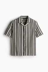 Camisa de manga corta con cuello resort y tapeta con botones. Diseño a rayas verticales en tonos gris y blanco.