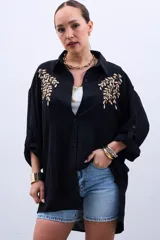 Camisa negra de mangas largas con puños abotonados y bordados dorados en el frente.