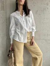 Camisa blanca de manga larga con detalles de broderie y calados en el frente y las mangas. Tiene cuello mao y cierre frontal con botones. Los puños son elásticos.