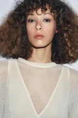 Vestido largo de punto ligero color crudo, con cuello redondo y mangas largas. Presenta un forro interior de tela satinada color beige claro que asoma en el bajo, creando un efecto de dos piezas.