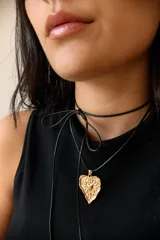 Collar con tiento encerado negro y dije dorado con forma de corazón texturizado.