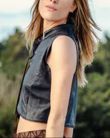 Chaleco corto negro de cuero ovino, con cuello mao y cierre frontal mediante tientos de cuero marrón que pasan por ojalillos metálicos.