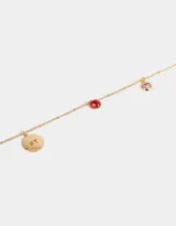 Collar corto dorado con cadena de eslabones y dijes colgantes: moneda dorada con letras NY grabadas, dos manzanas rojas esmaltadas y dije redondo dorado con corazón rosa.
