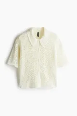 Camisa color crema de tejido crochet con cuello clásico, cierre frontal con botones y mangas cortas.