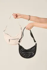 Cartera tipo baguette color crema, de ecocuero matelassé con cierre frontal y correa regulable.