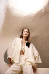 Saco de lino color crudo, de corte amplio, con solapas, bolsillos falsos y pin de guitarra en la solapa.