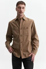 Sobrecamisa color marrón claro de twill de algodón, con cuello clásico, cierre frontal con botones a tono, dos bolsillos de parche con solapa abotonada en el pecho y mangas largas con puños abotonados.