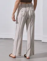 Pantalón de lino color beige con rayas verticales marrones, pretina ancha con punto smock y lazo ajustable, bolsillos verticales delanteros y bolsillos aplicados traseros.