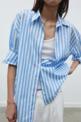 Camisa celeste y blanca a rayas verticales, de popelina, con cuello solapa, escote en pico y mangas largas.