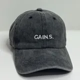 Gorro color beige con visera y bordado frontal con la palabra "GAINS" en color blanco.