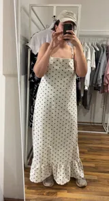 Vestido largo de algodón color blanco con estampado de lunares pequeños en color marrón. Presenta tirantes finos y escote pronunciado en la espalda. El ruedo tiene un volante con fruncido.