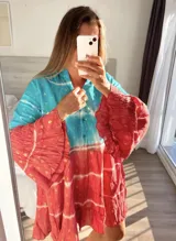 Vestido corto con estampado batik en tonos turquesa y rojo, con mangas largas acampanadas y cuello camisero.
