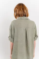 Vestido camisero corto color verde oliva, confeccionado en lino 100%. Tiene botones en la parte delantera, cuello camisero, mangas cortas con botón para arremangar y bolsillos laterales.