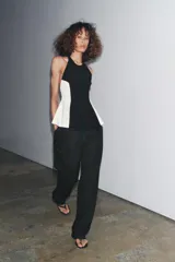 Top negro con cuello halter y espalda descubierta. Presenta detalle de combinación de tejidos en contraste con laterales blancos y bajo acabado en peplum.