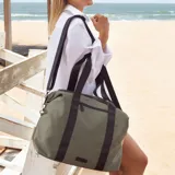 Bolso deportivo color verde militar, con asas cortas y correa larga regulable, ambas en color negro. Cuenta con cierre superior y bolsillo frontal con cierre.