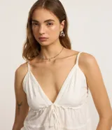 Blusa blanca de algodón y poliéster con breteles finos, escote en V con lazo ajustable y detalles de recortes decorativos.