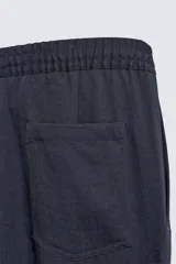 Pantalón negro de corte relajado con cintura elástica ajustable y pliegues en la parte delantera. Presenta bolsillos laterales y bolsillos traseros de parche.