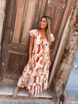 Vestido largo con estampado abstracto en tonos camel, naranja y blanco, con escote en V, mangas cortas con volados y falda con volados en el ruedo.