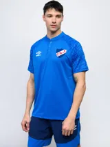 Remera polo de entrenamiento color azul marino, con cuello tipo henley de tres botones y mangas cortas. Presenta un patrón texturizado en los hombros y el escudo del Club Nacional de Football en el pecho izquierdo.