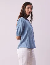 Blusa celeste de lyocell, con cuello a la base, escote en V y botones. Delantera con bolsillo y manga corta con terminación en punto smock.