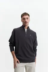 Sweater verde oliva de punto con cuello alto y cierre de medio cierre. Tiene puños y logo bordado en el pecho.