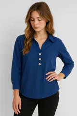 Blusa azul con cuello camisero, corte holgado, mangas 3/4 y cierre parcial con botones.