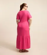 Vestido midi fucsia de algodón, con cuello redondo, mangas cortas, corte a la cintura y falda amplia con volantes.
