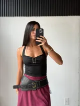 Top negro con breteles finos y escote halter. Presenta un aplique metálico rectangular en el centro del busto.