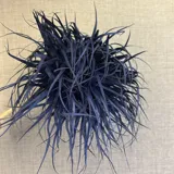 Broche decorativo de tela roja, con forma de pompón o flor, compuesto por tiras finas de material textil que le dan un gran volumen y textura.