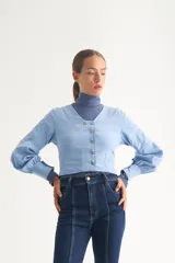 Blusa celeste de escote en V, con botonadura frontal cruzada y mangas largas abullonadas con puños ajustados.