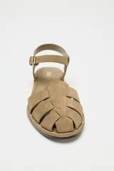 Sandalias cangrejeras planas de serraje color beige, con puntera redondeada y cierre de hebilla lateral ajustable.