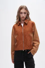 Chaqueta corta color marrón con detalles en color camel, de gamuza sintética, con cuello camisero, cierre frontal con cremallera y apliques de tachas plateadas.