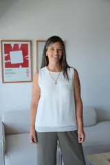 Musculosa blanca de corte holgado, sin mangas, con cuello redondo y un bolsillo pequeño en el pecho. El ruedo inferior presenta un detalle de encaje o puntilla calada.