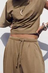Pantalón color marrón claro, de tiro medio, corte ancho y largo tobillero. Cuenta con cintura elástica ajustable con cordones y bolsillos laterales ocultos en la costura.