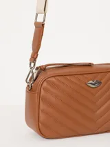 Bandolera color beige con diseño acolchado en forma de V y logo metálico dorado en forma de labios. Tiene correa larga ajustable y herrajes plateados.