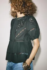 Blusa negra de algodón con cuello redondo y manga corta abullonada. Presenta bordados a tono y cierre en la espalda con abertura y botón.