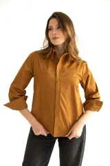 Camisa marrón de corte clásico, con cuello, mangas largas con puños abotonados, cierre frontal con botones al tono, bolsillo de parche en el pecho y ruedo redondeado.