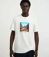 Remera de algodón color crema con cuello redondo y mangas cortas. Presenta un estampado rectangular con la imagen de un auto rojo en un paisaje y texto en la parte inferior.