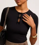 Blusa blanca de mangas cortas, confeccionada en Rib, con cuello redondo y lazos de terciopelo negros uniendo la abertura en la parte de abajo.