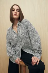 Camisa blanca con estampado de líneas verticales negras, de calce relajado, cuello clásico, abotonadura frontal y mangas largas con puños camiseros.