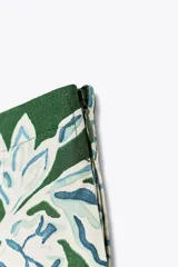 Falda midi de tiro medio con estampado floral en tonos blanco y celeste sobre fondo verde. Presenta detalle de tablas y cierre lateral con cremallera oculta.