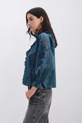 Camisa blanca de algodón con detalles de plumetí, puntillas, alforzas y bordados a tono. Tiene volados en el frente y mangas al codo abullonadas con elástico y volados.